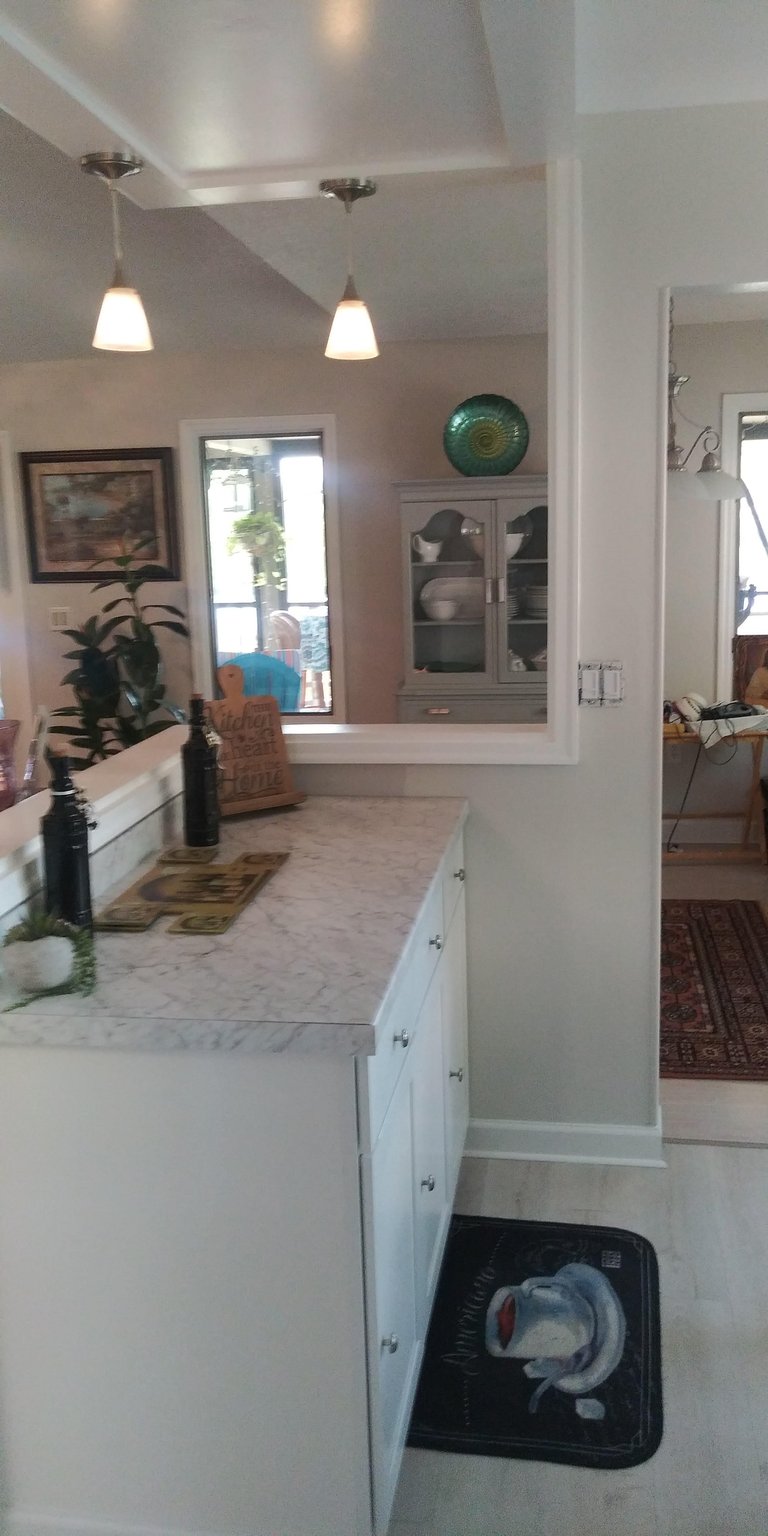 Modern kitchen interior with white cabinetry, pendant lighting, open floor plan, and views into adjoining dining room with green decorative plate