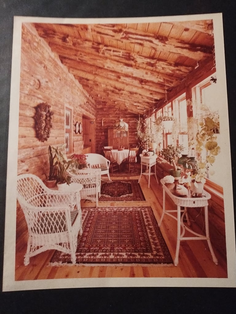 Vintage sepia-toned interior of a rustic log cabin with wicker chairs, patterned rugs, and period furnishings