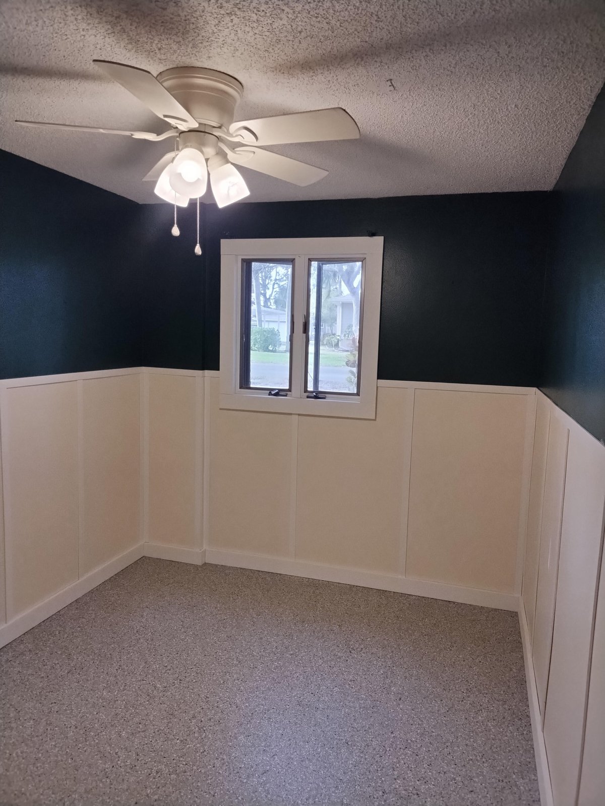 Empty room with cream wainscoting on lower walls, dark blue upper walls, ceiling fan, and double French doors with outdoor view