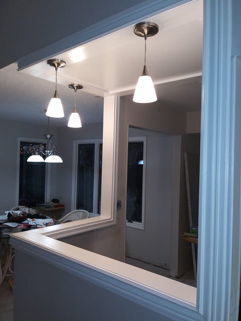 Modern kitchen pass-through window with three white pendant lights hanging above the counter and white-framed opening