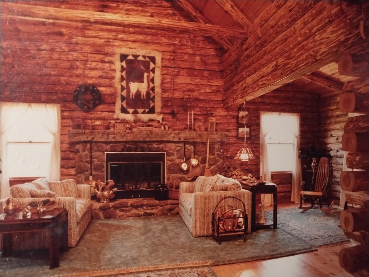 Rustic log cabin interior with fireplace, striped armchairs, decorative artwork, and traditional wood furnishings