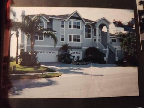 Two-story white modern house with large garage, palm trees, and driveway on a sunny day