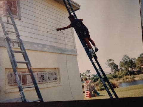 Person climbing down a tall ladder leaning against the side of a white house