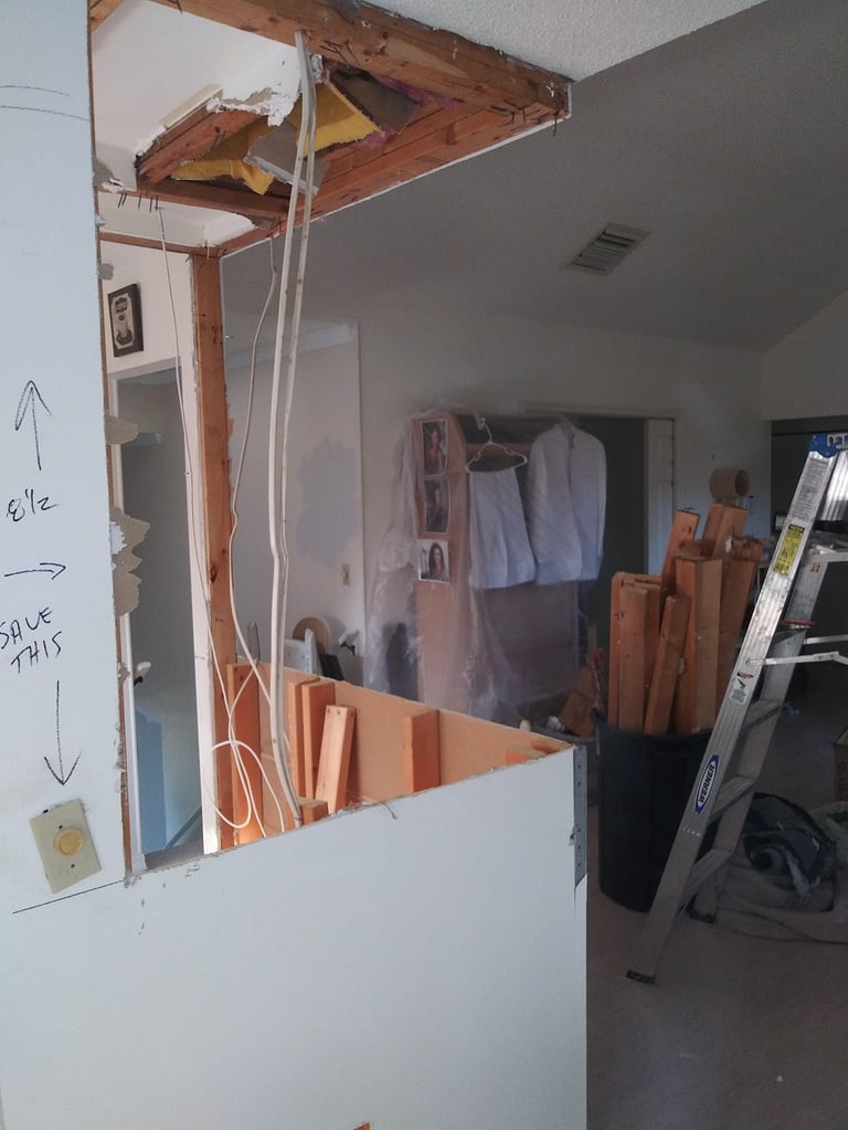 Partially demolished interior wall showing exposed wooden framing, drywall, and electrical wiring with construction materials visible