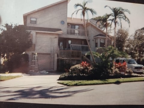 A two-story residential house with a garage, palm trees, and landscaping along a quiet street