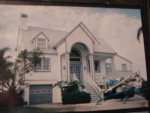 White two-story house with arched entrance and gray garage door, with construction equipment parked in front